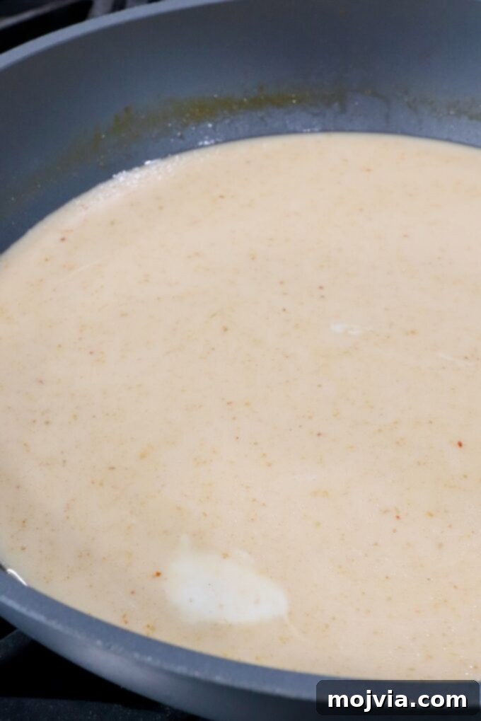 Creamy coconut milk being poured into a large pot of simmering broth, creating the rich, white base for the Thai coconut potsticker soup.