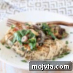 Whole30 Garlic Mushroom Spinach Chicken 2 Sliced mushroom spinach chicken breast on plate with copper fork, sitting on gold and white patterned napkin