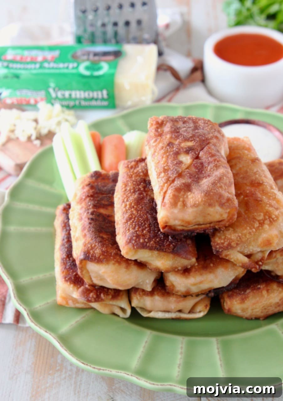 A vibrant green plate holds a generous pile of golden-brown Buffalo chicken egg rolls, accompanied by fresh, crisp carrot and celery sticks in the background, ready for dipping.
