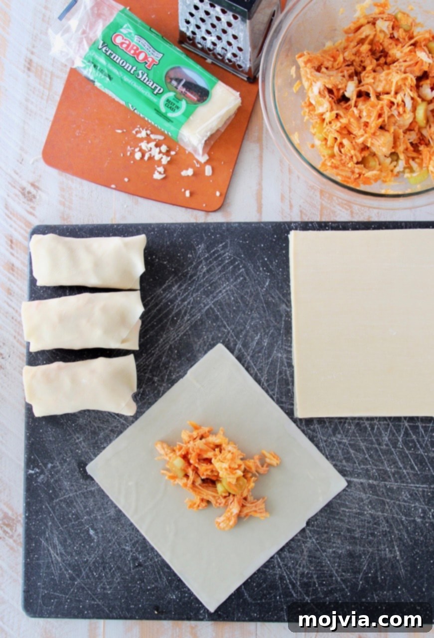 A clear, step-by-step visual of buffalo chicken egg roll preparation, showing the filling being placed onto the wrapper and the initial fold, highlighting the simplicity of the assembly process.