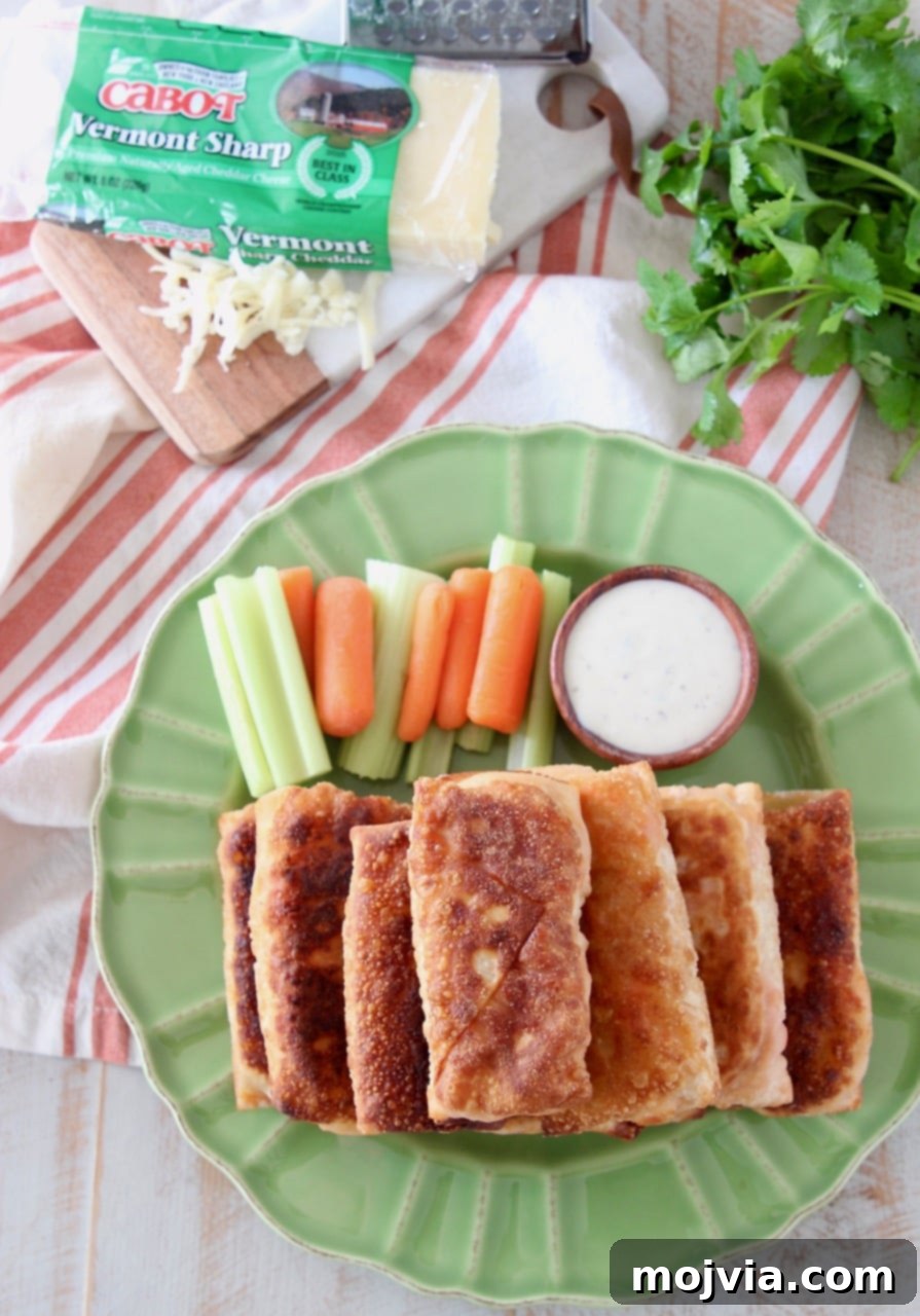 An overhead shot showcasing a meticulously arranged stack of freshly pan-fried buffalo chicken egg rolls on a vibrant green plate, with crunchy carrot and celery sticks, and a small wooden ramekin of creamy ranch dressing placed strategically for dipping.