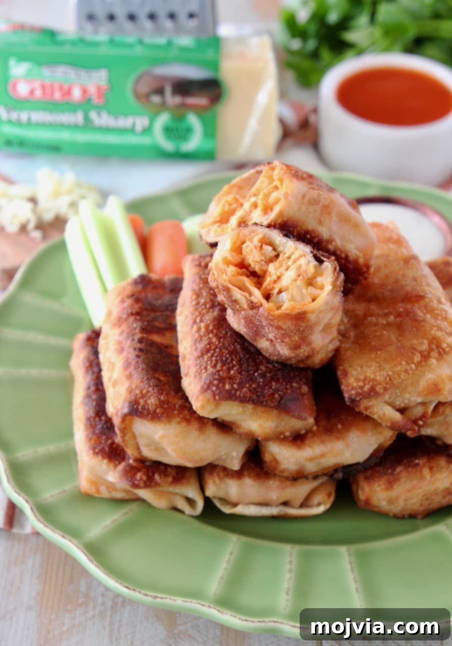A close-up view of Buffalo chicken egg rolls stacked on a green plate, with the top egg roll halved to reveal its delicious, cheesy, and spicy interior. Perfect for showcasing the mouthwatering filling.