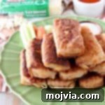 Buffalo chicken egg rolls piled up on a green plate with celery and carrots on the plate and a small wooden bowl filled with ranch dressing