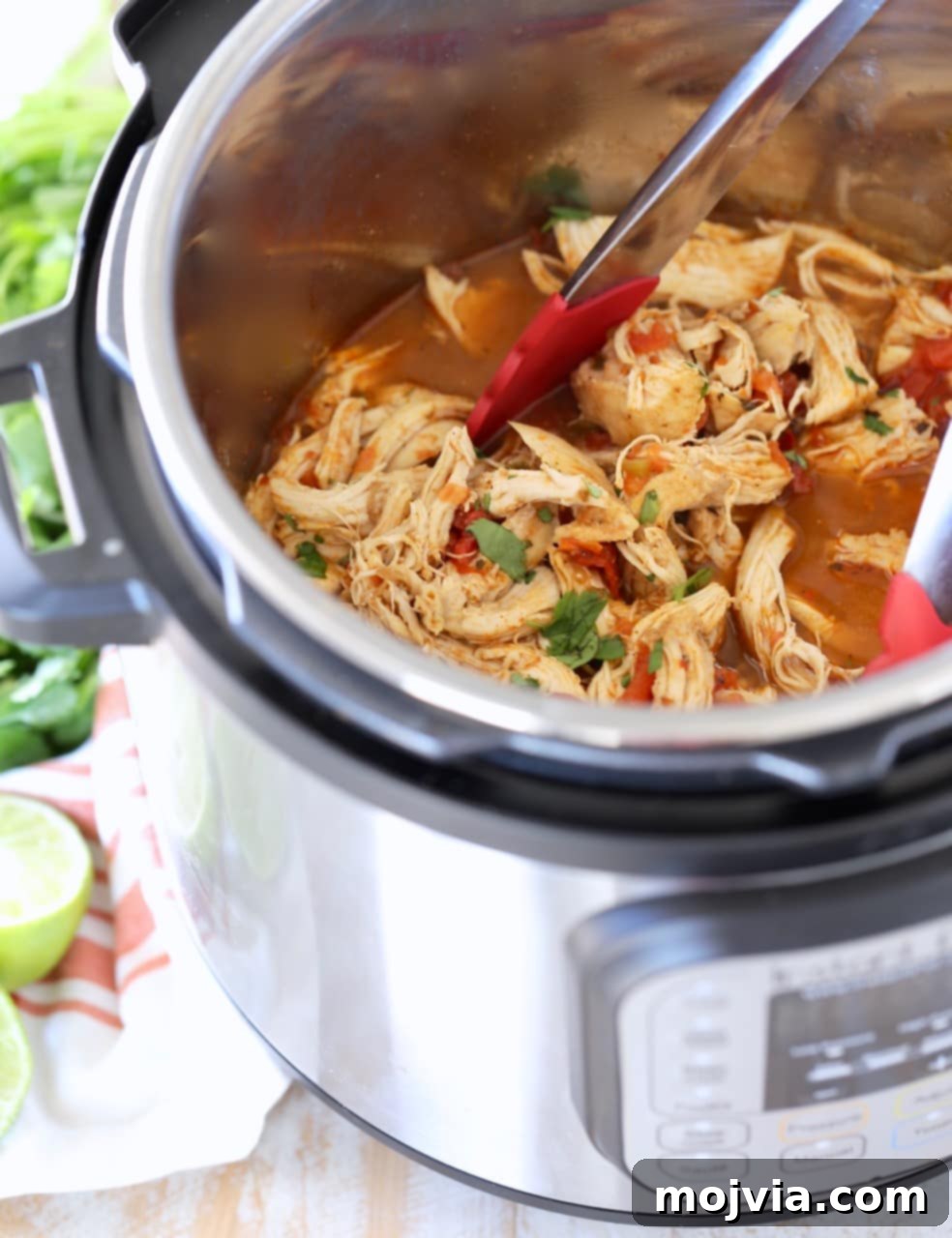 Shredded taco chicken in Instant Pot with red tongs and cilantro