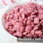 Close-up of red velvet puppy chow in a white bowl, showing the powdered sugar coating