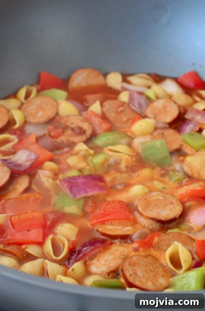 Spicy Cajun One-Pan Pasta 5 Sliced sausage, peppers, onions, and pasta shells simmering in a rich tomato broth in a large skillet.