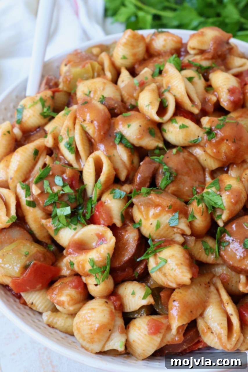 Spicy Cajun One-Pan Pasta 7 Cooked pasta with sausage and bell peppers in a large white bowl, garnished with fresh herbs.