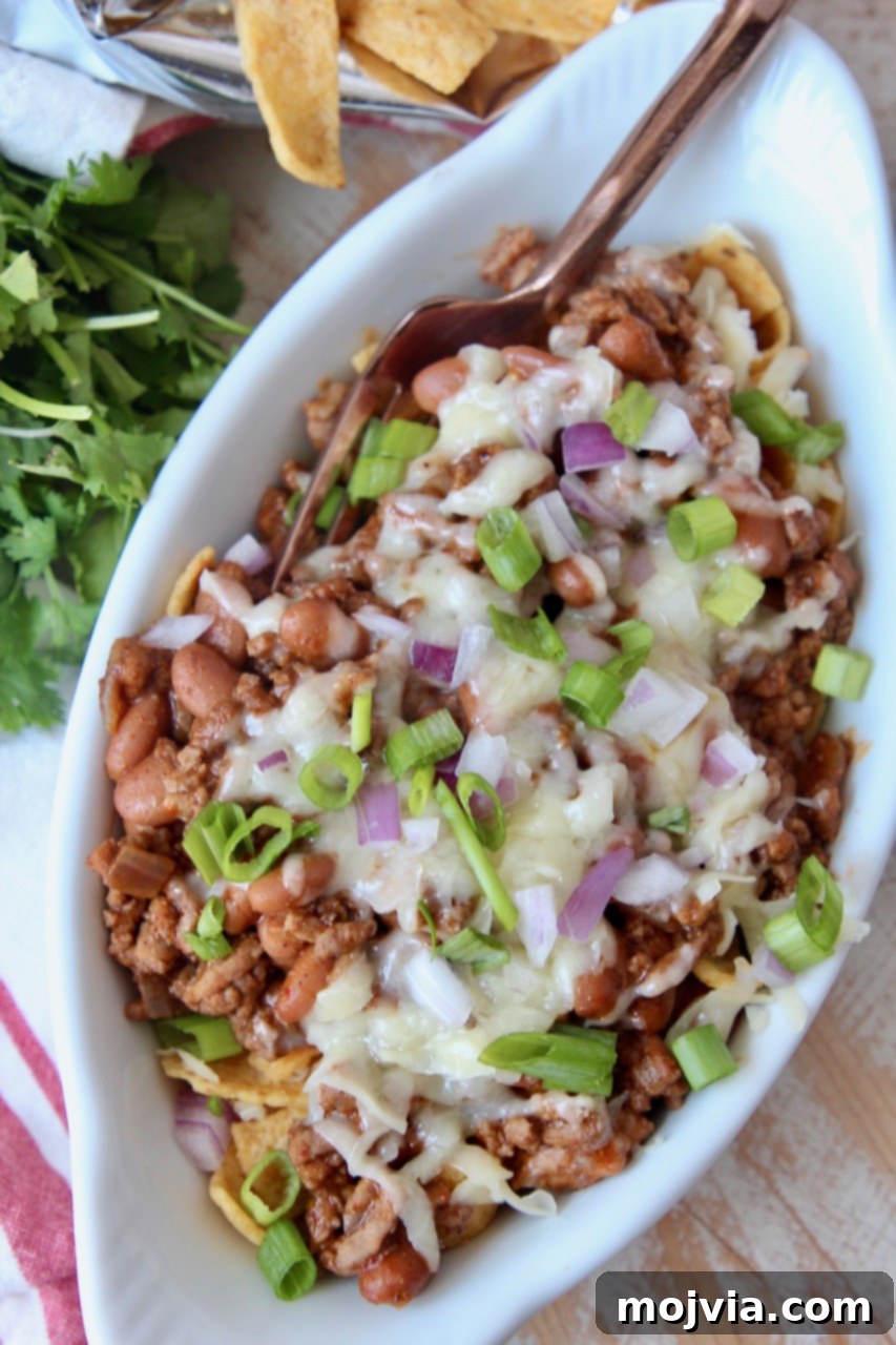 Tex-Mex Chili Crunch 5 An oval white bowl filled with Frito Chili Pie, garnished with diced green onions