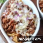 frito chili pie topped with cheese and diced red onion