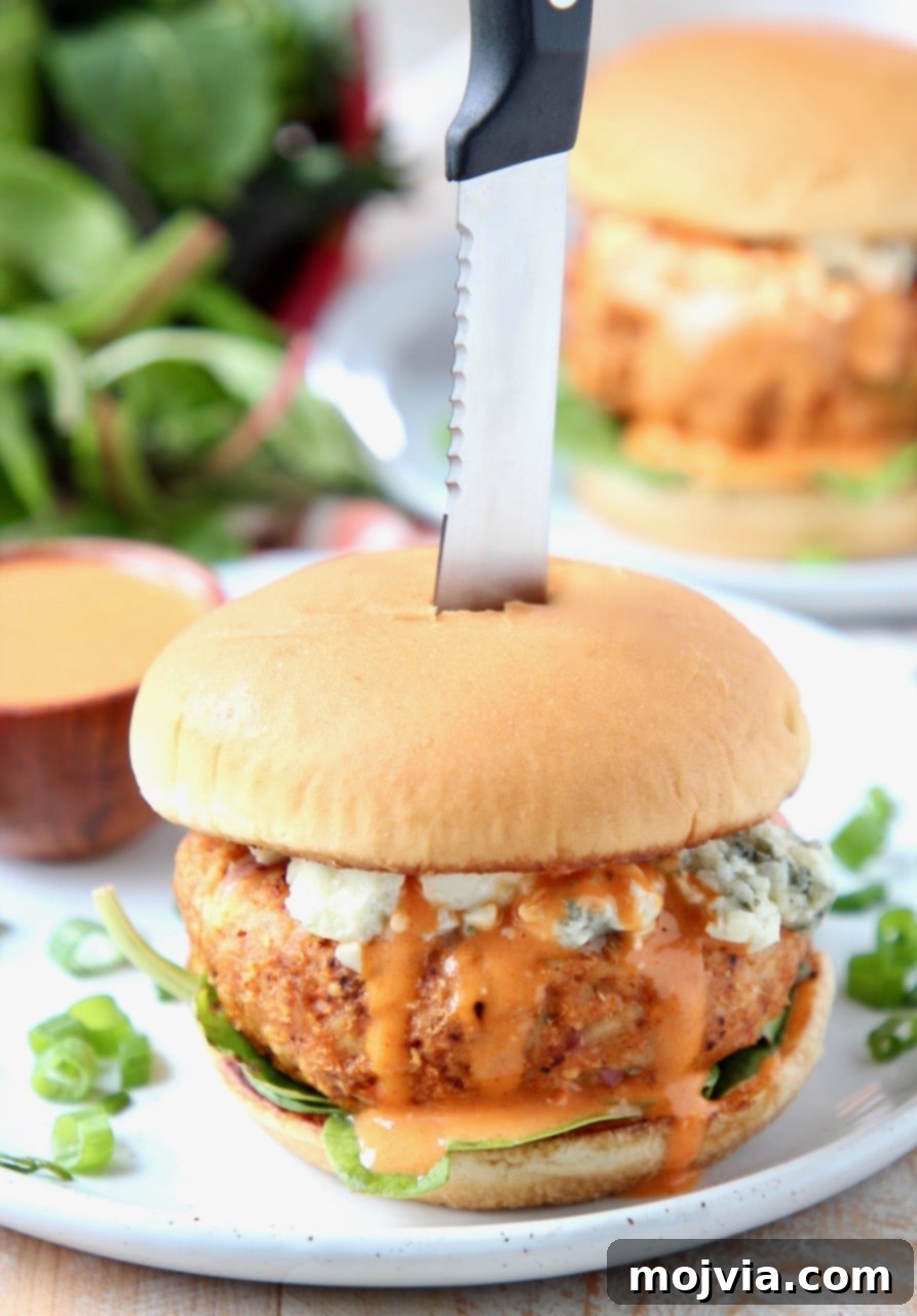 Fiery Buffalo Chicken Burgers 2 Buffalo chicken burger on plate, topped with blue cheese crumbles with knife in the middle of the burger