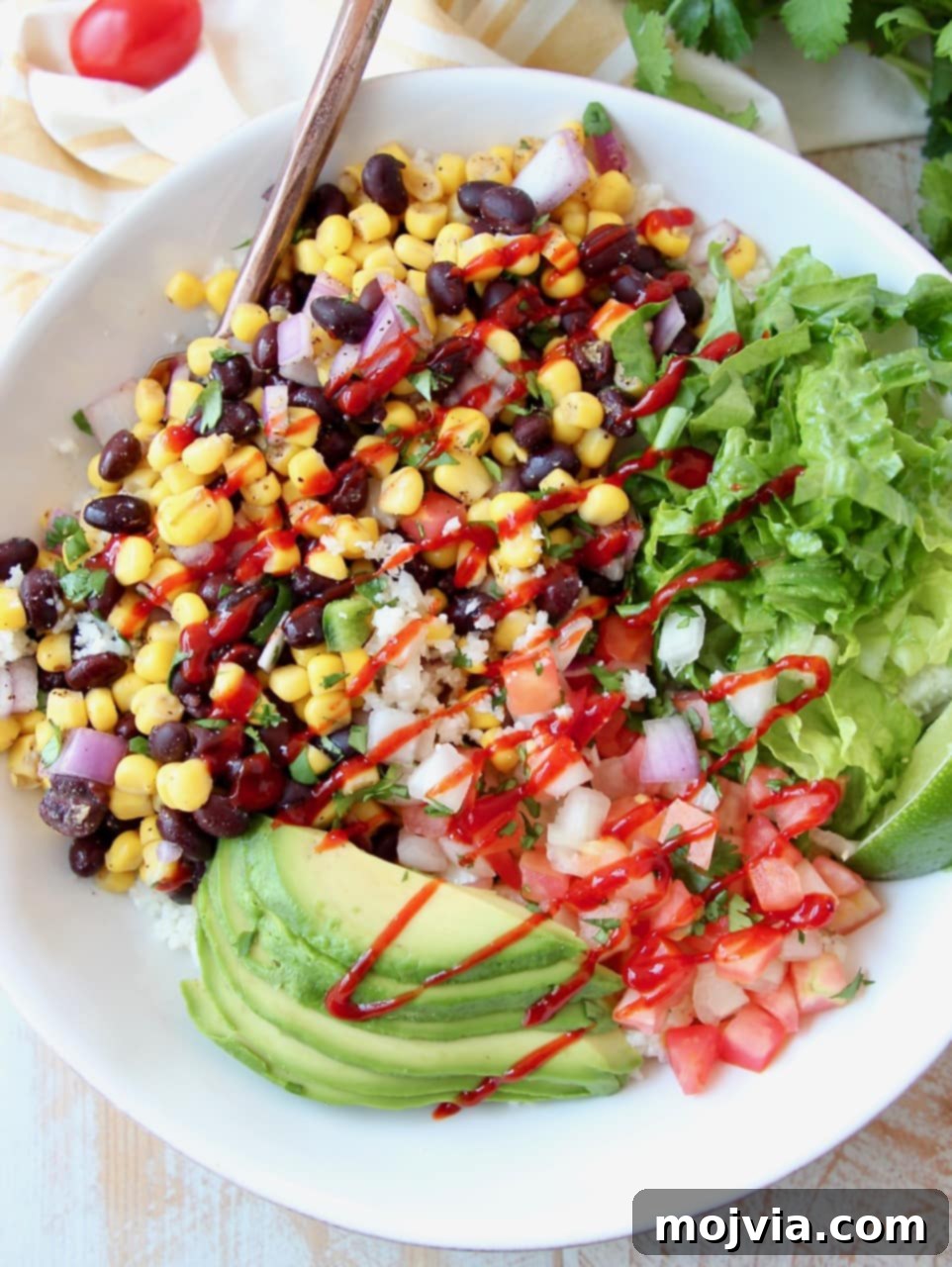 Plant-Powered Burrito Bliss 4 Burrito bowl with avocado, corn, tomatoes and black beans, topped with a drizzle of hot sauce in a white bowl