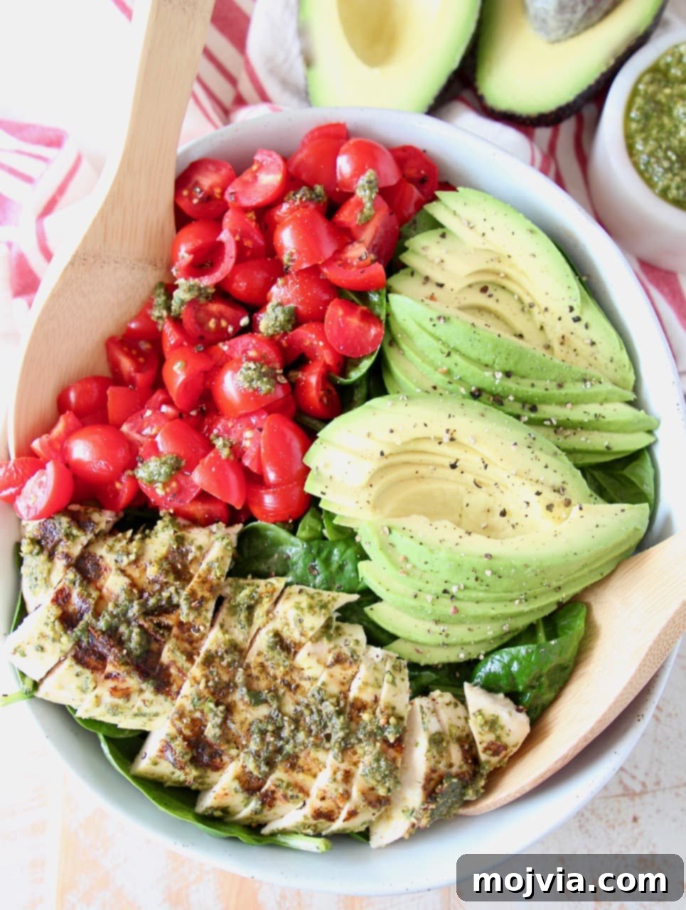Pesto Grilled Chicken Avocado Salad 4 Sliced pesto chicken, sliced avocado, diced tomatoes and spinach in large bowl with wooden serving spoons