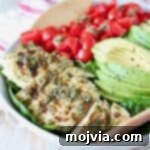 Sliced pesto chicken in bowl with sliced avocado and diced cherry tomatoes
