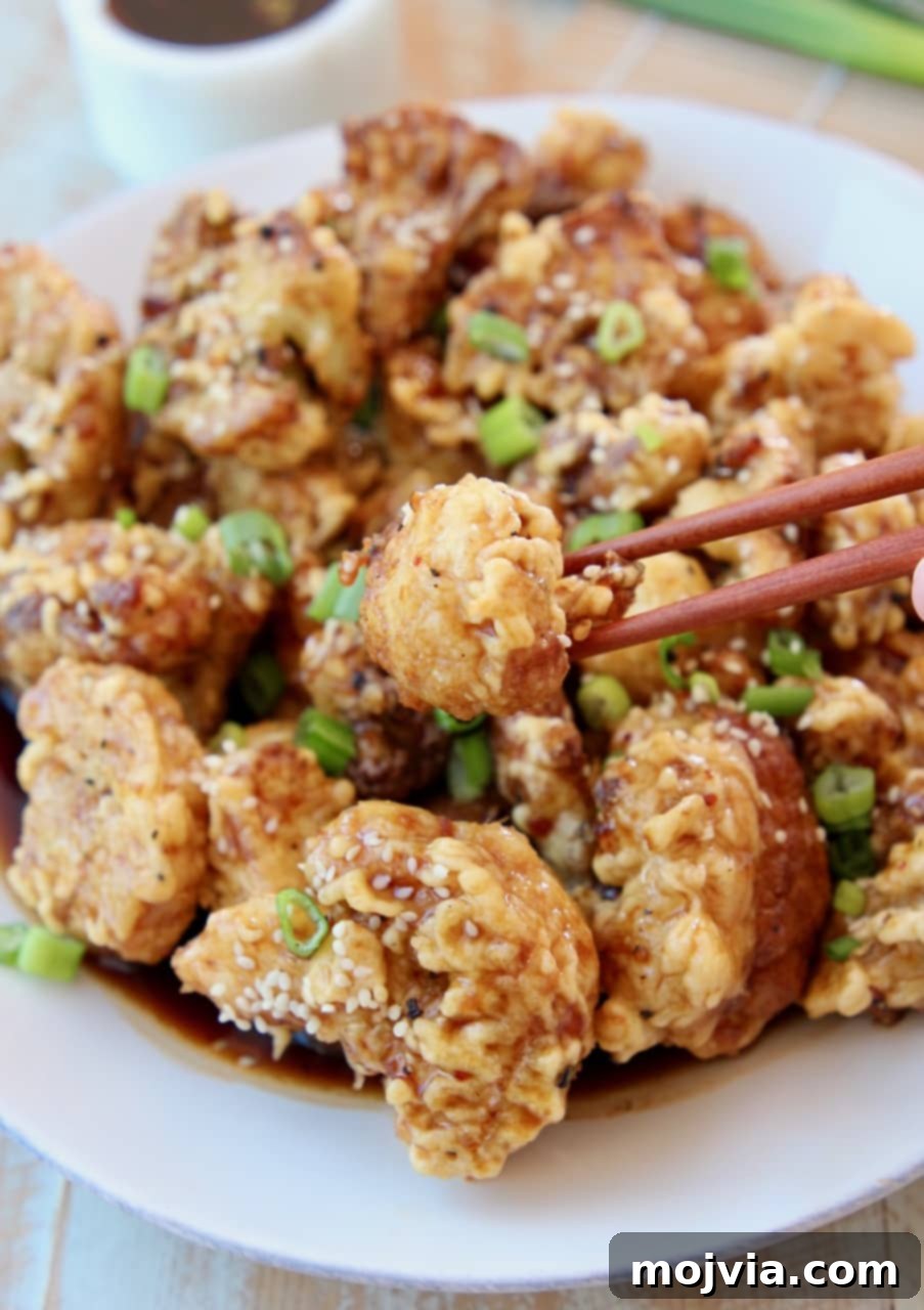Gochujang Glazed Cauliflower Wings 2 Korean fried cauliflower on plate with chopsticks picking up one piece of cauliflower