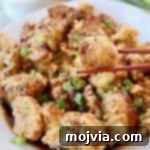 Piece of fried cauliflower in chopsticks, held over plate of fried cauliflower with Korean BBQ sauce
