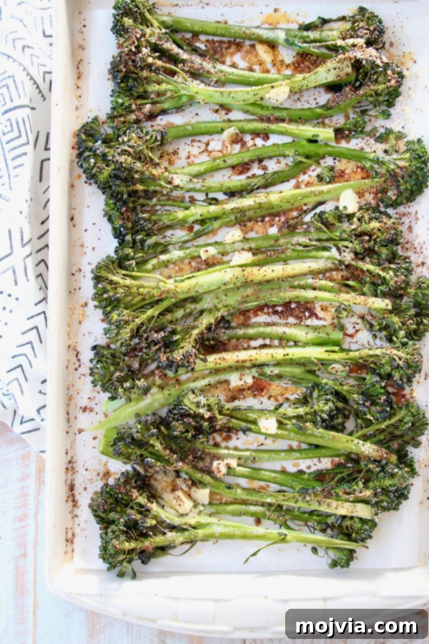 Golden Roasted Garlic Parmesan Broccolini 5 Fresh broccolini and garlic cloves tossed with olive oil and seasoning on a baking sheet, ready for roasting.