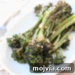 Golden Roasted Garlic Parmesan Broccolini 6 Close-up of roasted broccolini on a white plate with garlic and parmesan