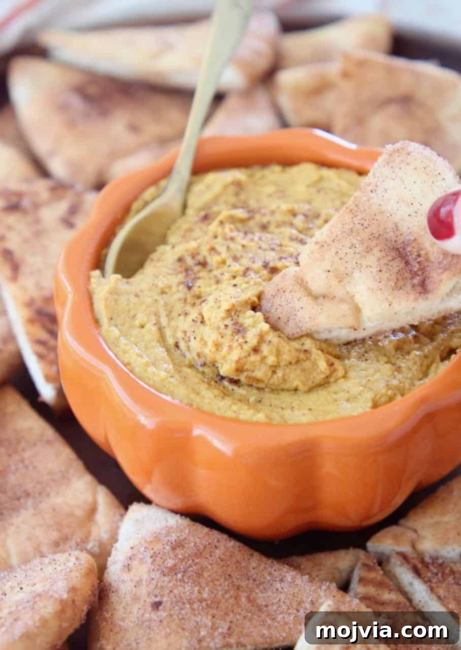 Pumpkin hummus in orange bowl with pita chip being dipped in the hummus