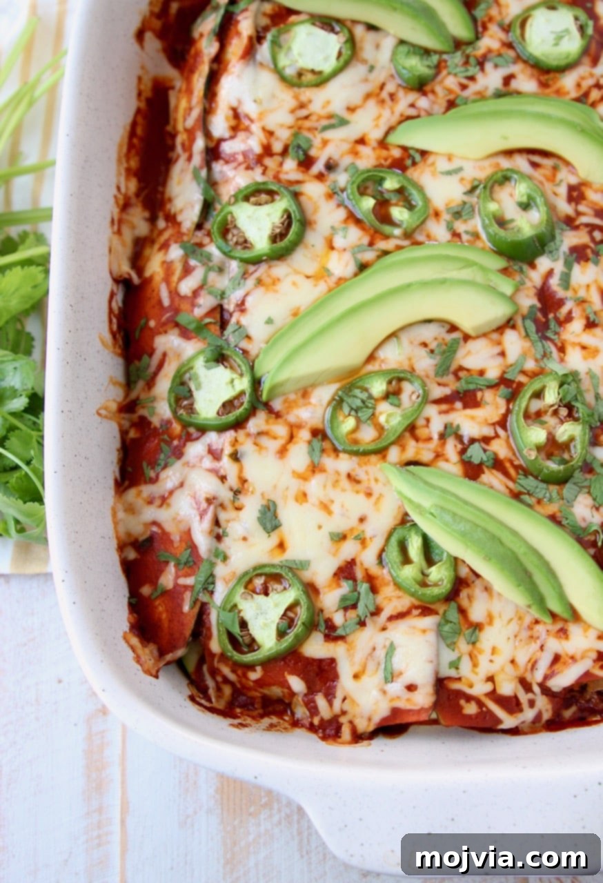 Overhead shot of enchiladas covered in red sauce and cheese in baking dish topped with avocado and jalapenos
