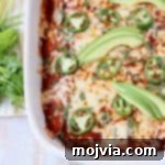 Overhead shot of enchiladas in casserole dish topped with sliced avocado and jalapenos
