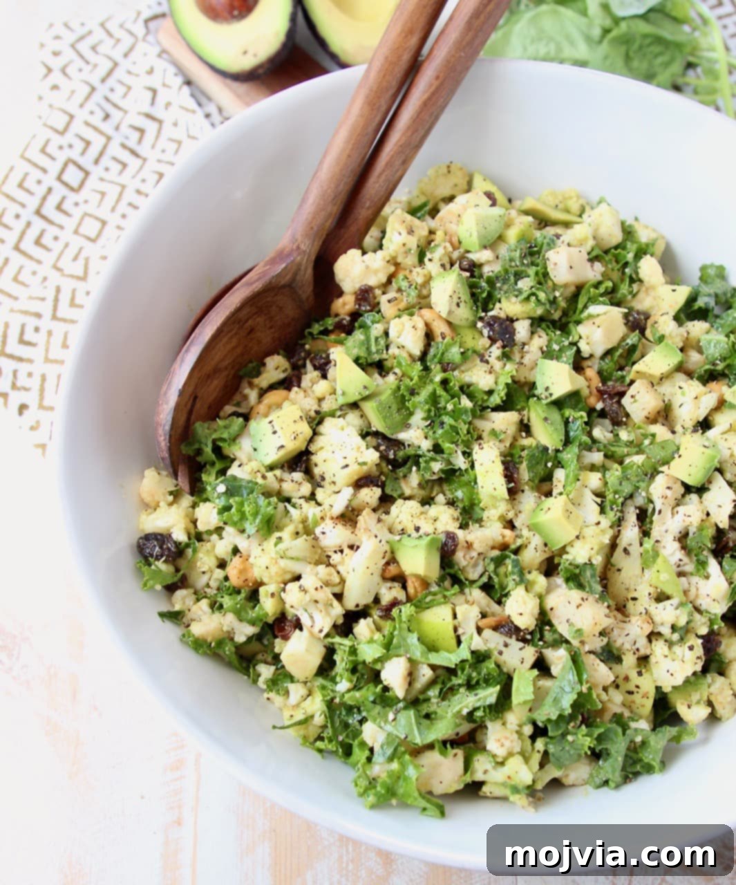 Overhead shot of cauliflower salad with chopped kale and avocado in large white bowl