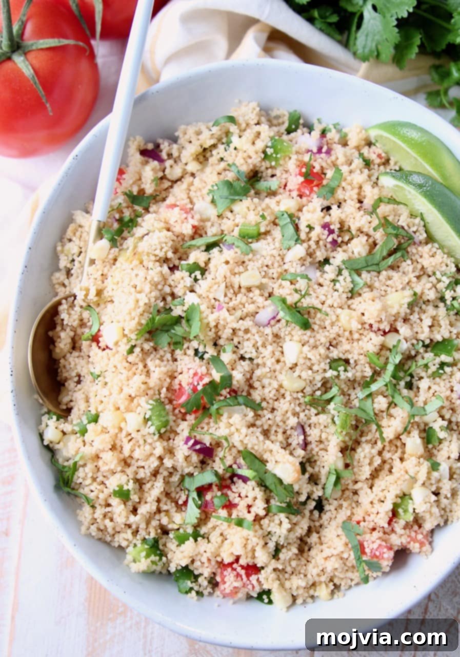 Overhead view of a beautiful bowl of cooked couscous mixed with fresh cilantro, diced tomatoes, and sliced limes, ready to be served as a healthy and flavorful side dish.