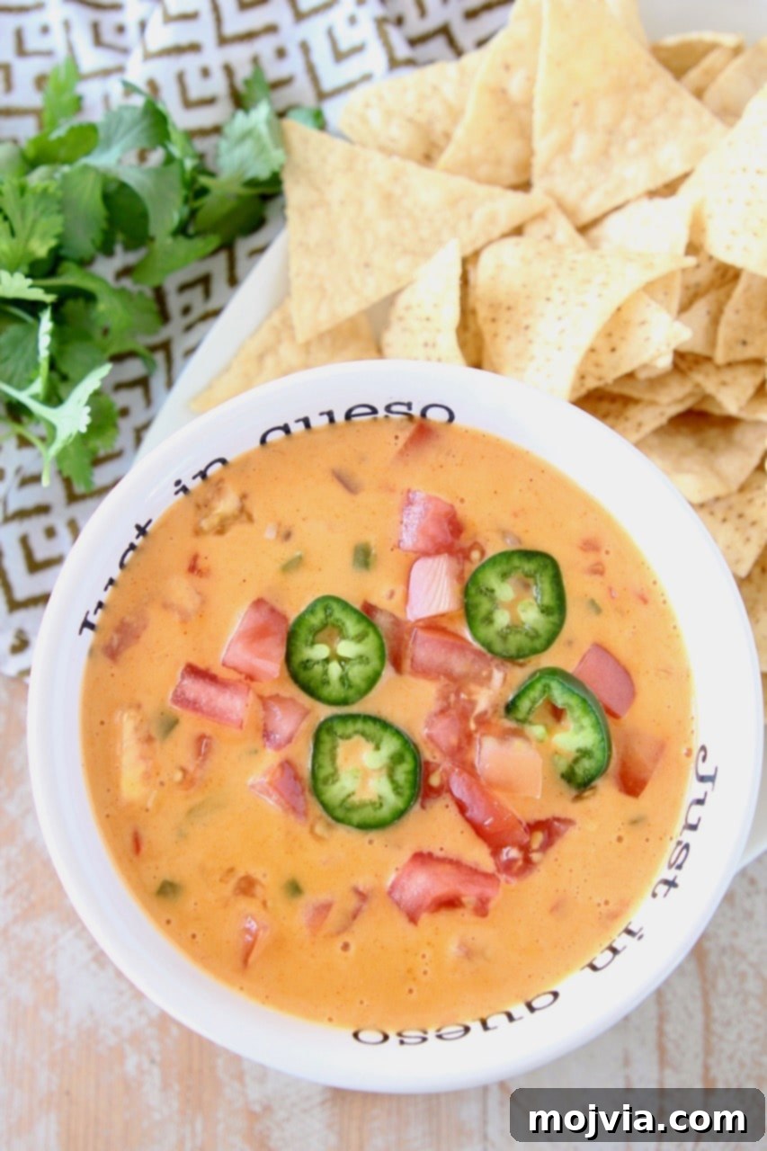 Zesty Buffalo Cheese Dip 2 A rich, creamy Buffalo Queso Dip in a white bowl, garnished with fresh diced tomatoes and vibrant green jalapeño slices, ready to be served.