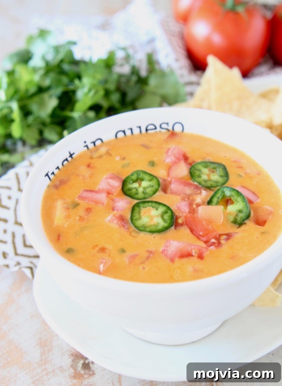 Zesty Buffalo Cheese Dip 4 A perfectly portioned white bowl of Buffalo Queso Dip, elegantly topped with vibrant diced tomatoes and thinly sliced jalapeños, resting on a rustic wooden surface, inviting you to dip in.