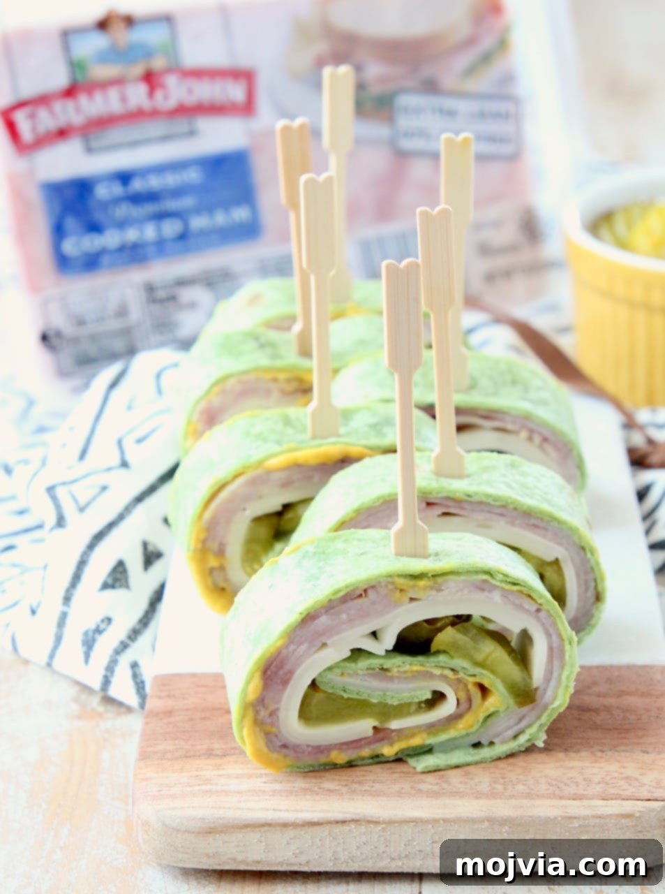 Pinwheel sandwich with ham, cheese, pickles and mustard, with toothpick in each piece, on a cutting board, ready for serving