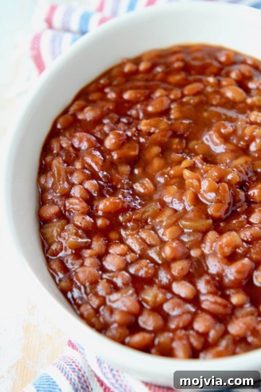 Dad's Legendary BBQ Baked Beans 4 A close-up shot of rich BBQ baked beans in an oval serving bowl, ready to be enjoyed.