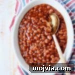 Baked beans in oval bowl with serving spoon in the bowl