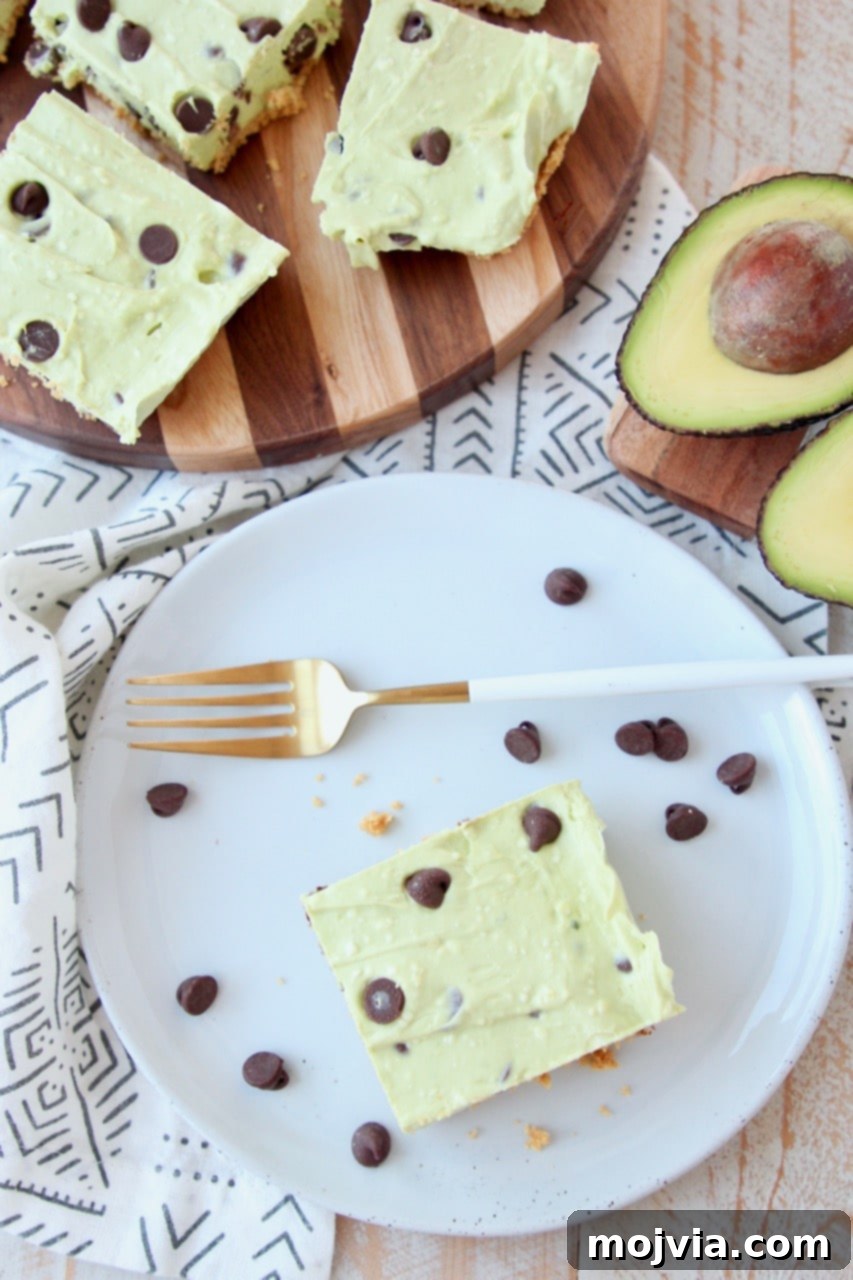 Effortless Avocado Bliss Bars 3 Overhead shot of vibrant avocado cheesecake bars on a plate and cutting board with chocolate chips and a halved avocado, highlighting the fresh ingredients.