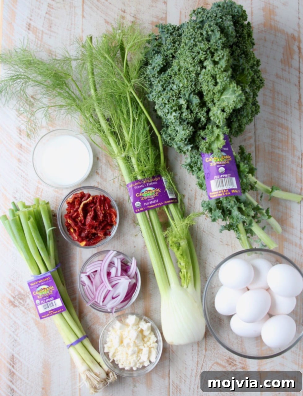 Sun-Kissed Mediterranean Frittata 4 Collection of fresh ingredients for Mediterranean Vegetable Frittata recipe on a wooden board, including fennel, kale, eggs, and feta.