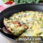 Close-up of a slice of vegetable frittata being lifted out of a skillet with a silver spatula, showcasing its vibrant layers.