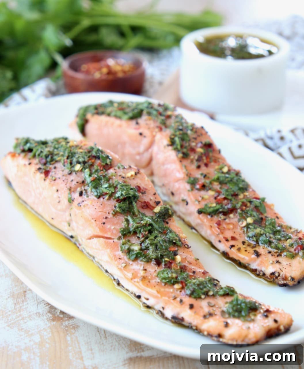 Two filets of grilled salmon on a white plate topped with chimichurri sauce
