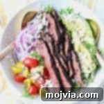 Grilled steak on top of salad in a white bowl with gold salad serving spoons