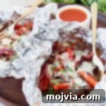 Cheesesteak foil packs with side of buffalo sauce in bowl and gold fork in foil pack
