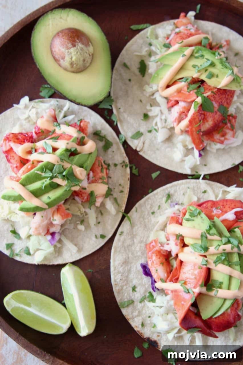 Decadent Lobster Tacos 3 Overhead shot of lobster tacos arranged on a wooden serving tray, accompanied by lime wedges and half an avocado, emphasizing the fresh ingredients and vibrant colors.