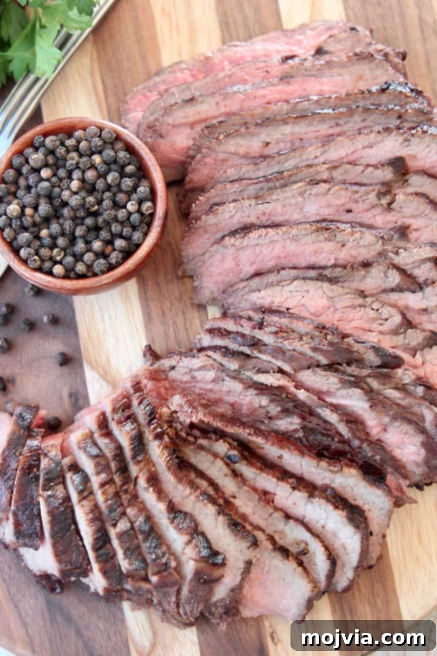 Epic Tri Tip Marinade Blend 2 Perfectly sliced tri tip steak on a rustic wood cutting board, garnished with fresh black peppercorns and herbs, emphasizing its juicy, tender texture.