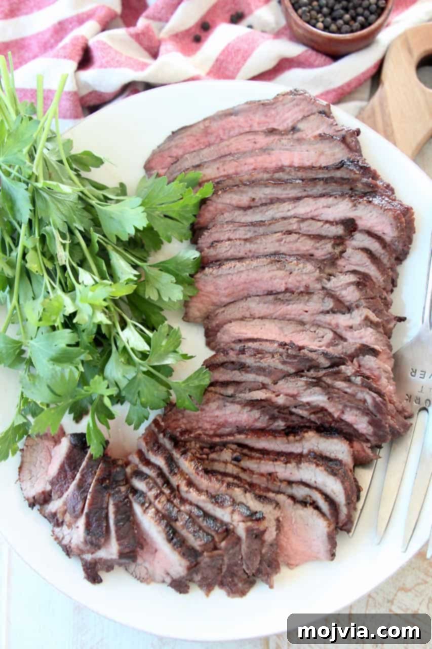Epic Tri Tip Marinade Blend 3 A serving of perfectly sliced tri tip steak on a white plate, garnished with fresh parsley, ready to be enjoyed.