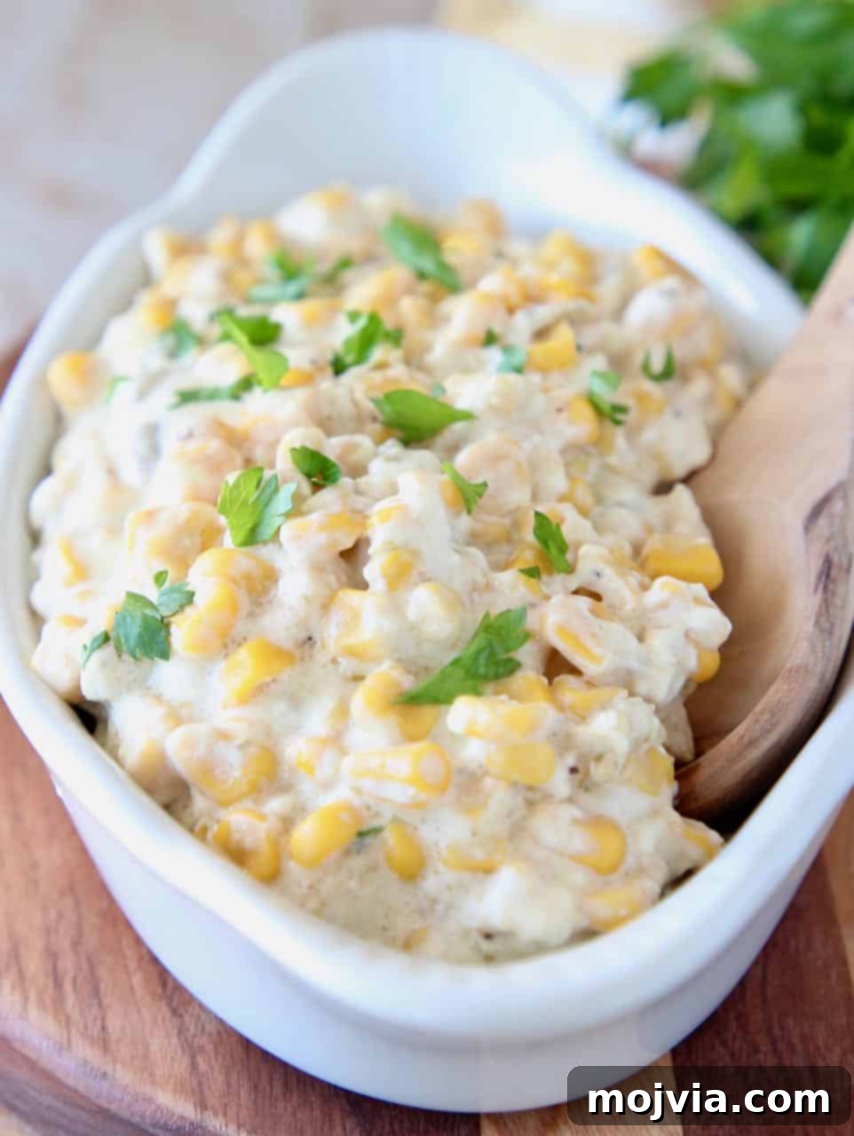 Velvety Slow Cooker Creamed Corn 2 Creamed corn in serving dish with wooden spoon, garnished with fresh herbs