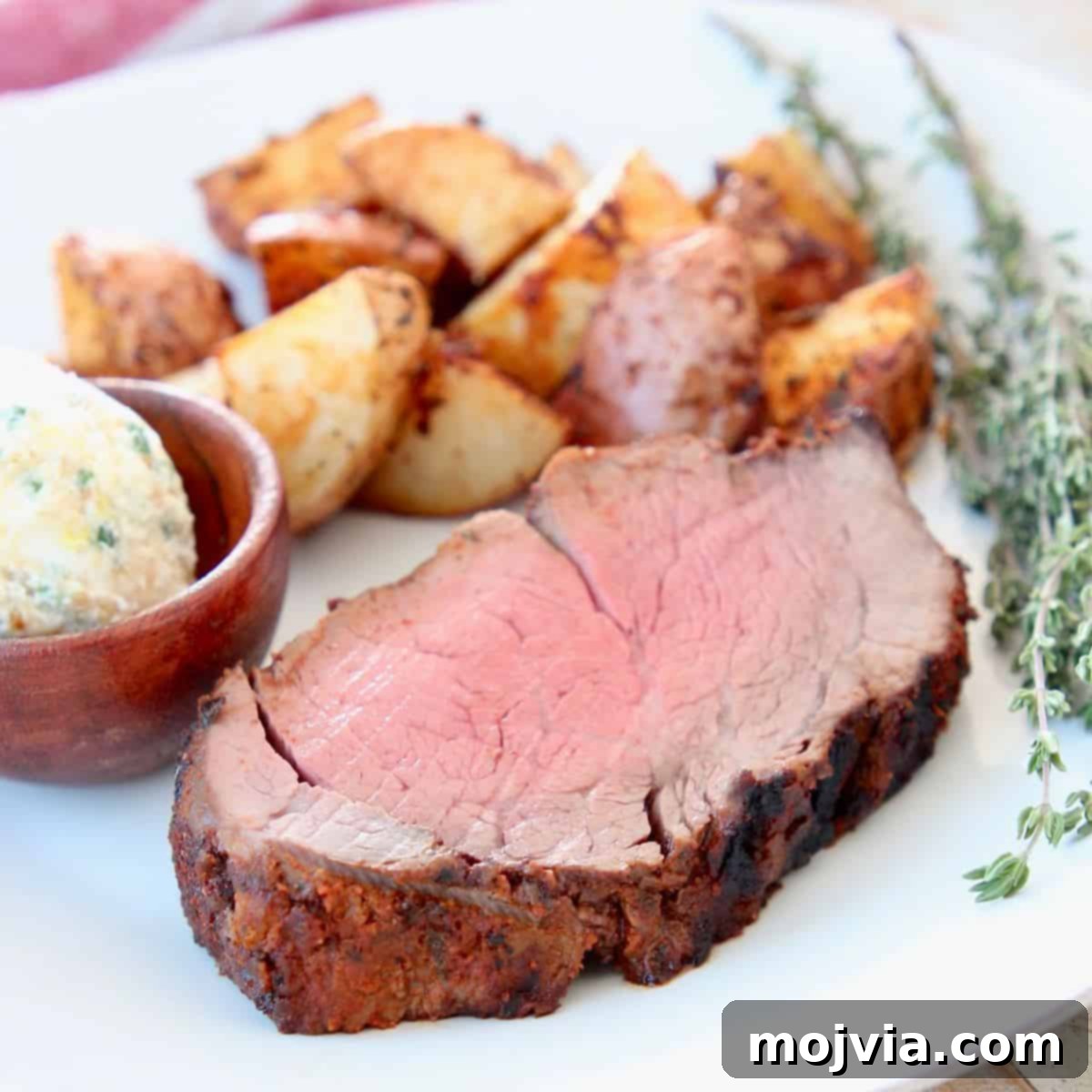 Spicy Crusted Beef Tenderloin 2 Slice of blackened beef tenderloin on plate with potatoes and herb butter in wood ramekin