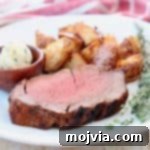 Spicy Crusted Beef Tenderloin 5 Slice of beef tenderloin on plate with fresh herbs and potatoes