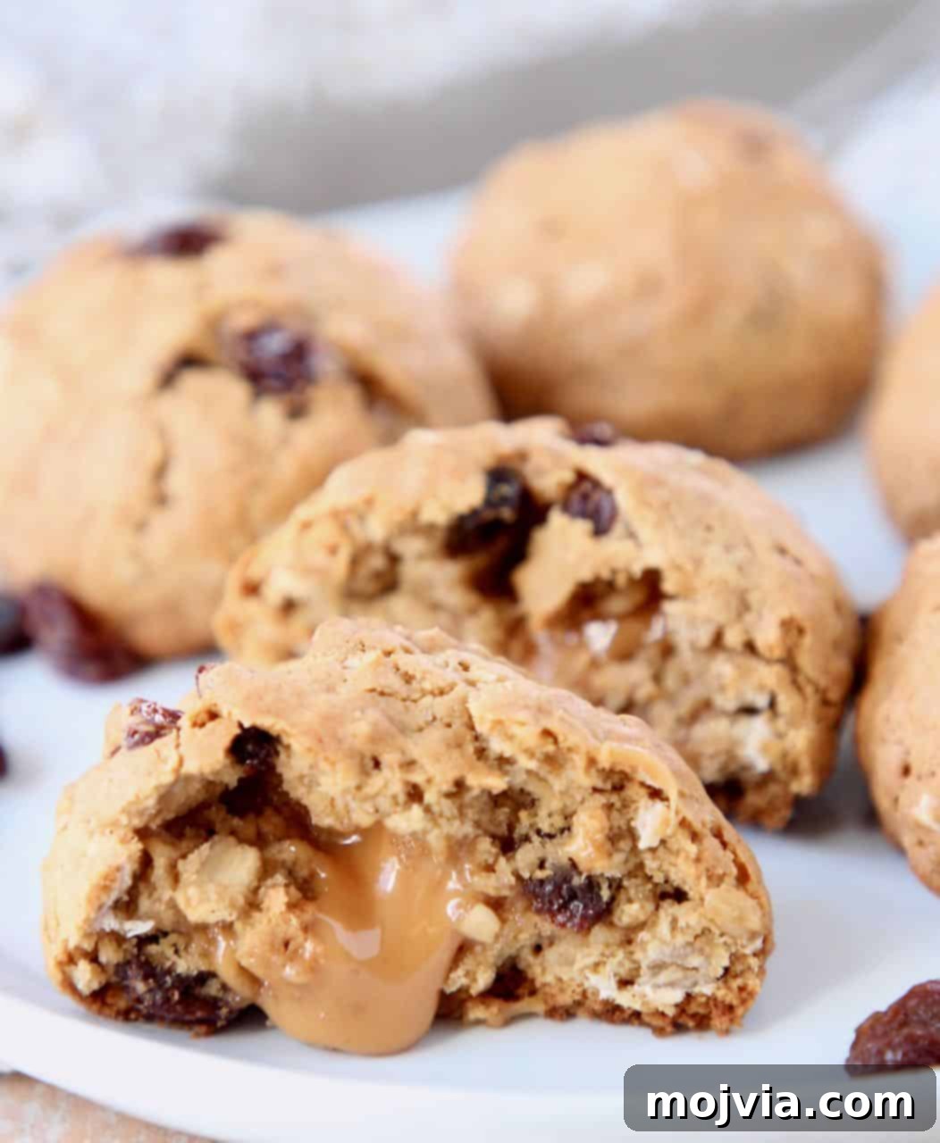 Caramel Core Oatmeal Raisin Cookies 5 A close-up of a single oatmeal raisin cookie, perfectly sliced in half, proudly displaying its rich, molten caramel filling. The golden-brown exterior and visible oats hint at its irresistible texture.