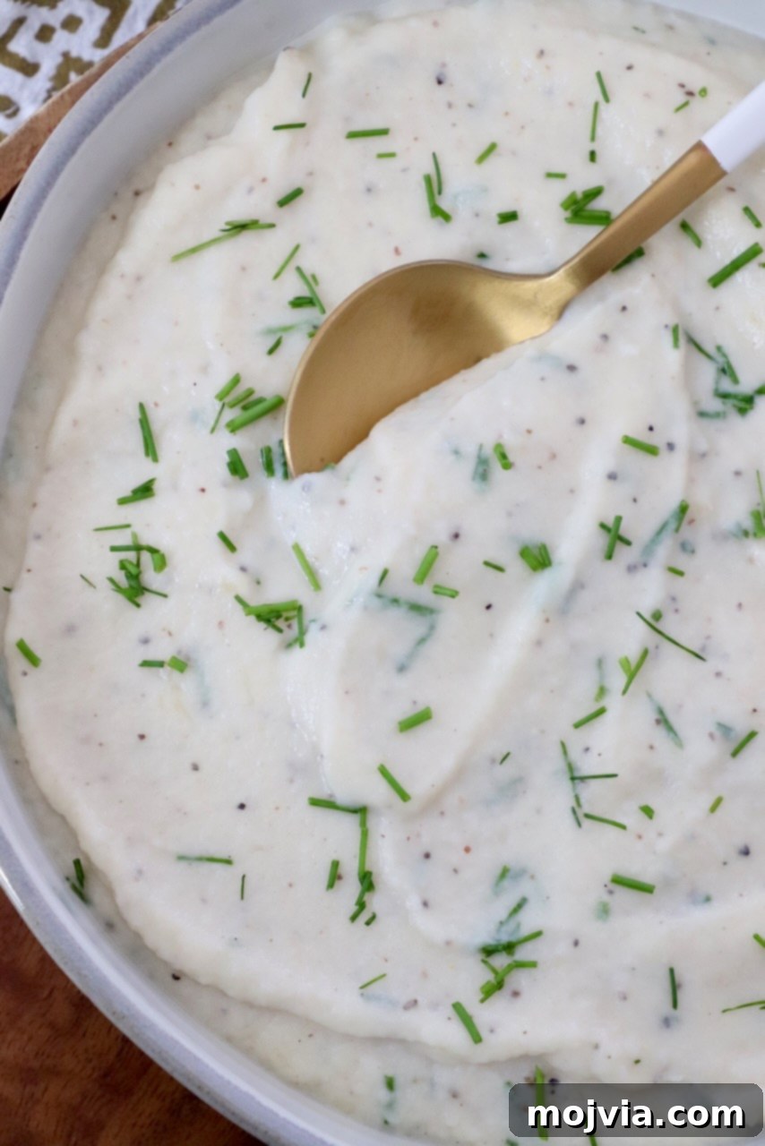 Creamy Cauliflower Mash 2 Creamy mashed cauliflower in a bowl, garnished with fresh chopped chives and a serving spoon.