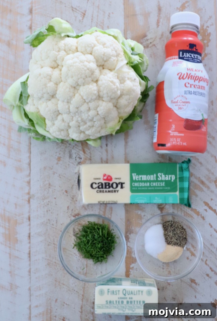 Creamy Cauliflower Mash 3 Fresh ingredients for making mashed cauliflower laid out on a white wooden board, including a head of cauliflower, butter, heavy cream, cheddar cheese, and chives.