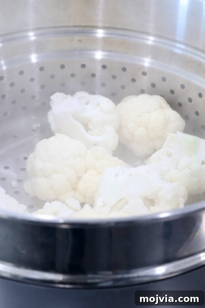 Creamy Cauliflower Mash 4 Cauliflower florets steaming in a steamer basket set inside a large pot.
