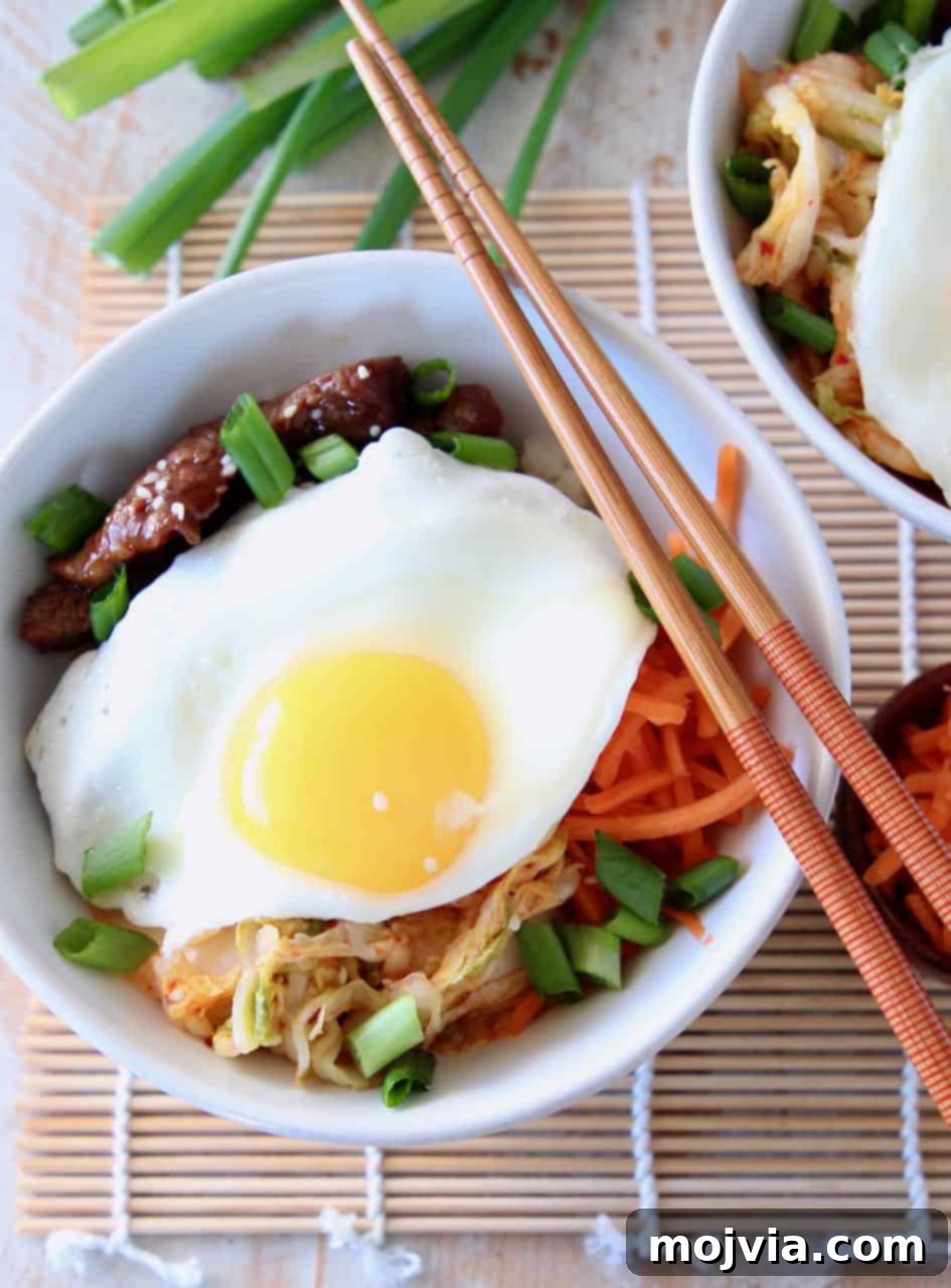 Korean BBQ Cauliflower Rice Bowl topped with a fried egg with chopsticks and green onions