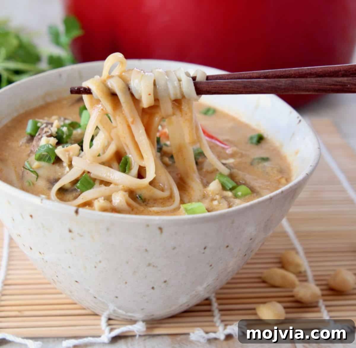 One Pot Creamy Thai Peanut Noodle Soup 3 Chopsticks pulling noodles out of a bowl of soup