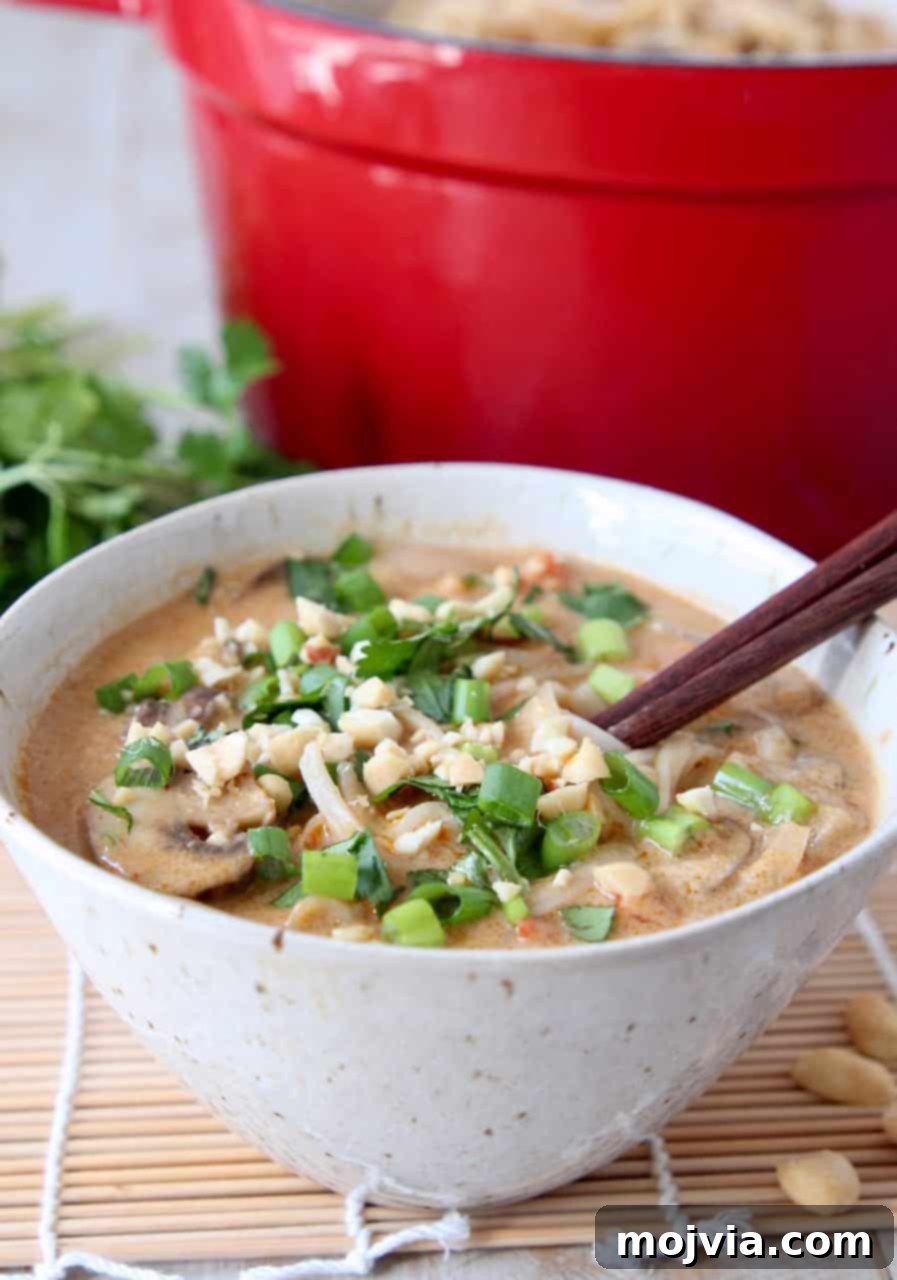 One Pot Creamy Thai Peanut Noodle Soup 4 Bowl of thai noodle soup with large red pot behind it